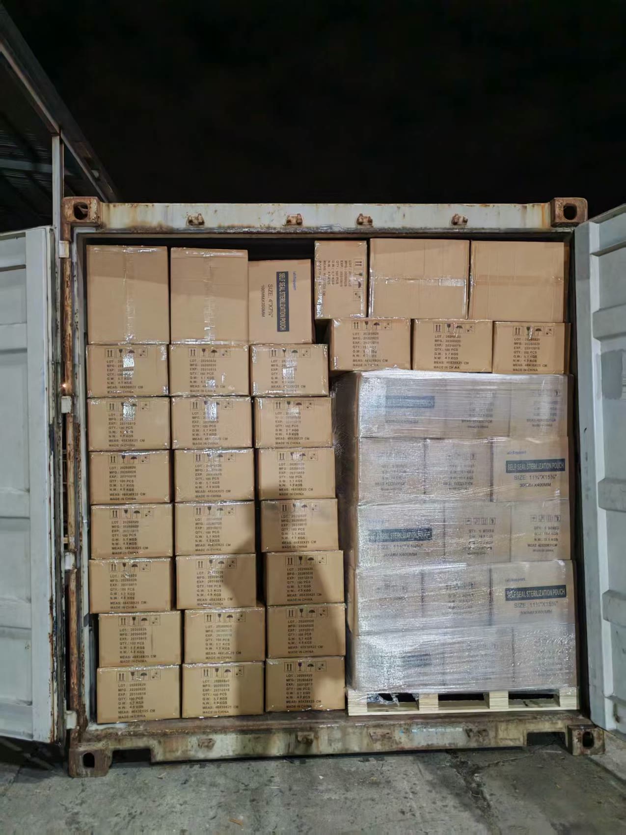 Container two, loaded after dark: stacked cartons beside a pallet wrapped in stretch film